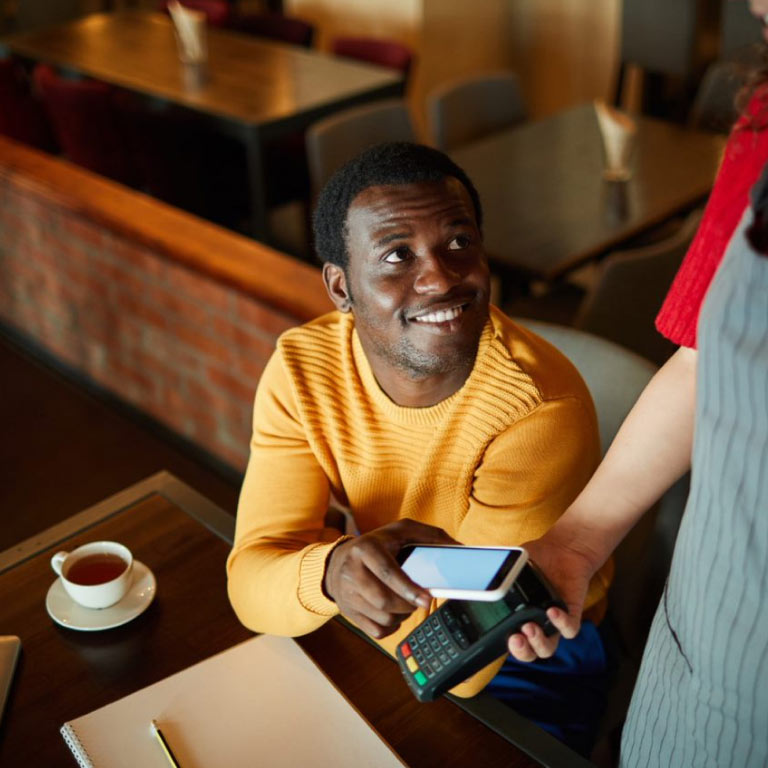 A young man at a café, interacting with a waitress and paying for his bill using his cell phone.