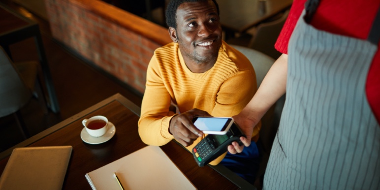 A young man at a café, interacting with a waitress and paying for his bill using his cell phone.