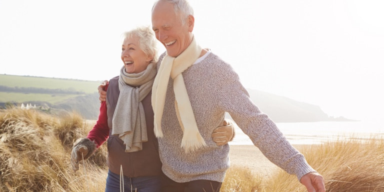 An older white male and female wearing warm clothes holding each other while hiking up a gentle incline.