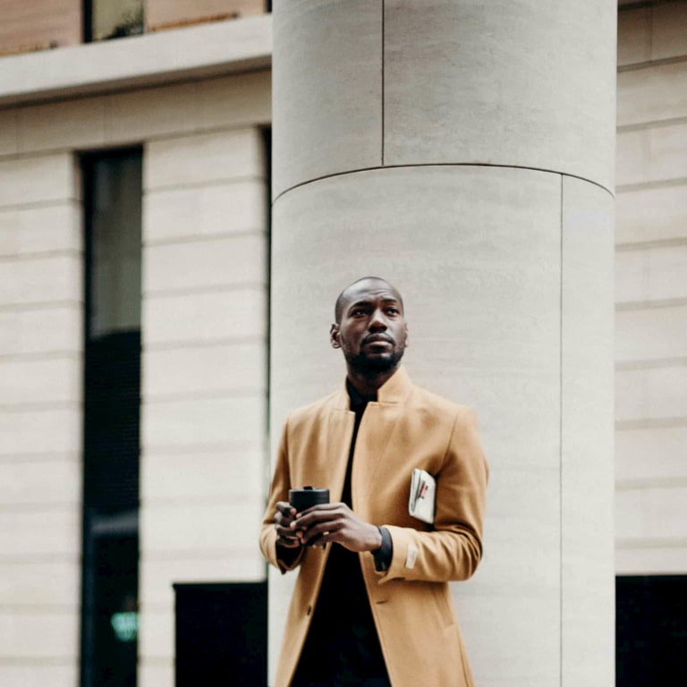 Momentum Investment Portfolios A businessman standing in front of a white building holding a takeaway coffee, with a folded newspaper under his arm.
