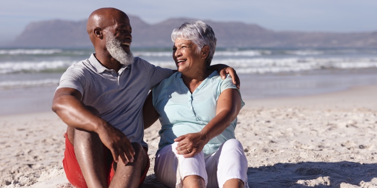 An elderly couple sitting on the beach enjoying their retirement years.