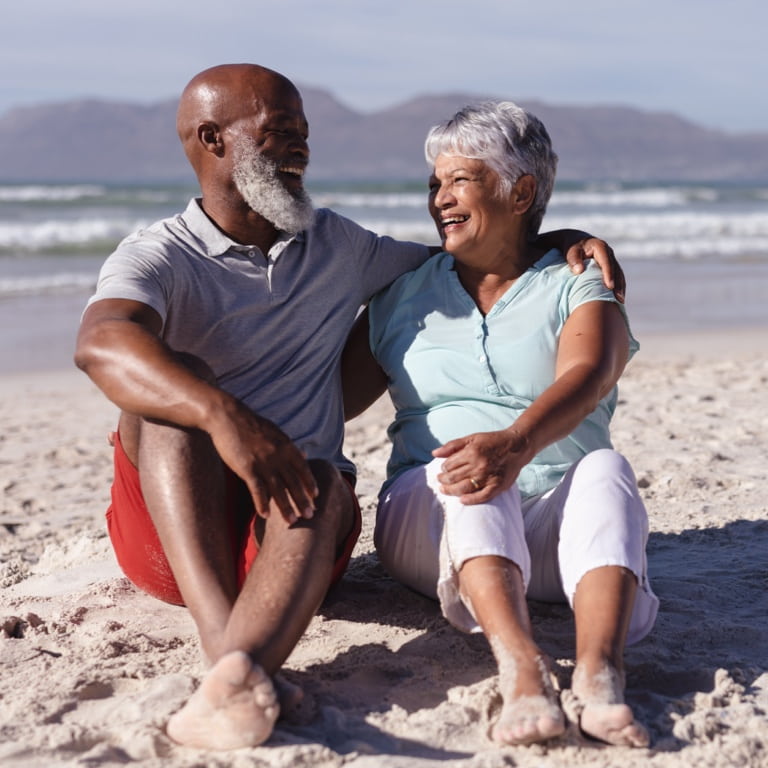 An elderly couple sitting on the beach enjoying their retirement years.