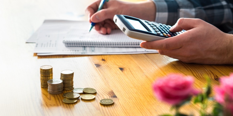 Close-up image of a man’s hands holding a calculator while taking notes.