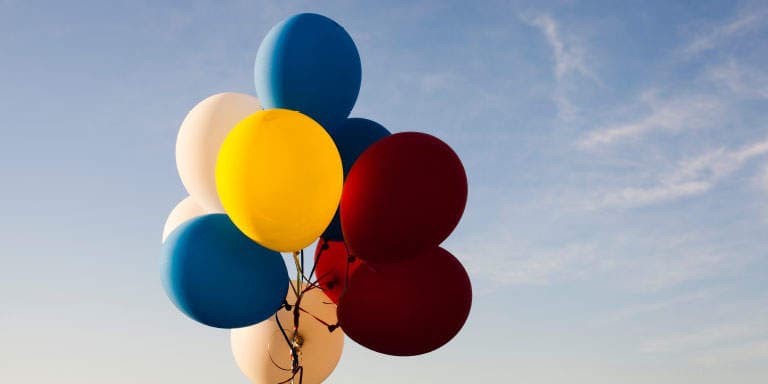 Two red balloons stand out from the rest of a bunch of multi-coloured balloons flying in the sky.