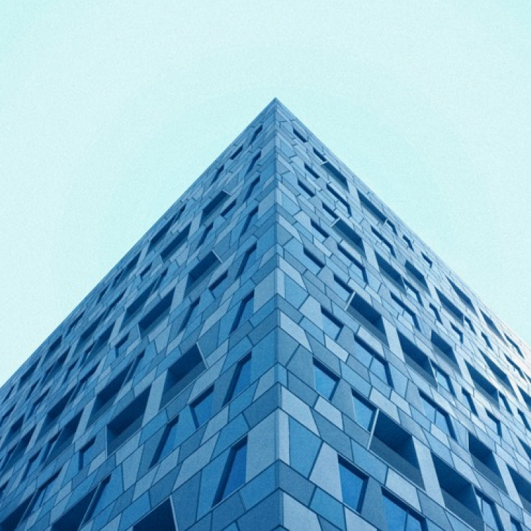 Top portion of a glass and steel pyramid structure - the design features a geometric grid of triangular glass panels framed by metal beams, creating a symmetrical pattern that converges to a point at the top.