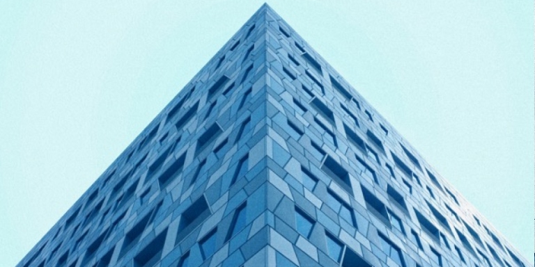 Top portion of a glass and steel pyramid structure - the design features a geometric grid of triangular glass panels framed by metal beams, creating a symmetrical pattern that converges to a point at the top.