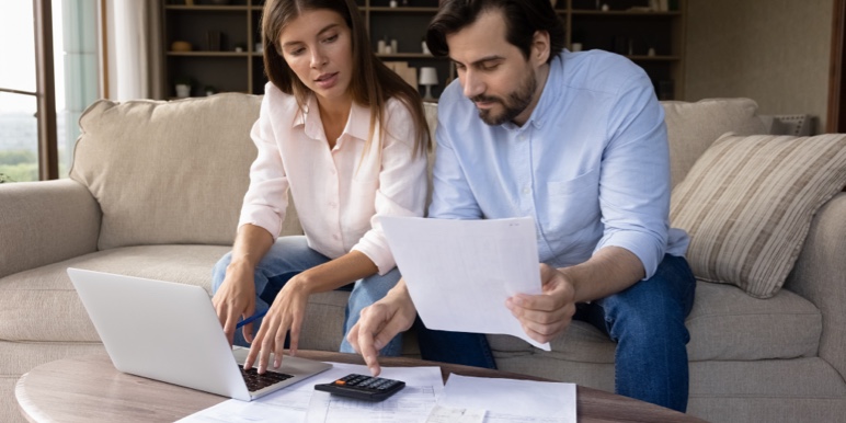 Couple looking concerned sitting in front of a table with a laptop and documents.