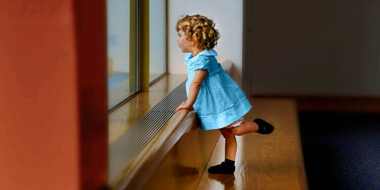 A girl toddler in a blue dress looking out the window.