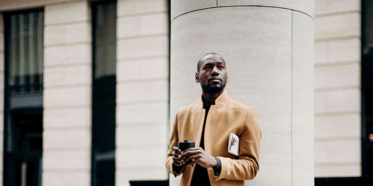 Momentum Investment Portfolios A businessman standing in front of a white building holding a takeaway coffee, with a folded newspaper under his arm.