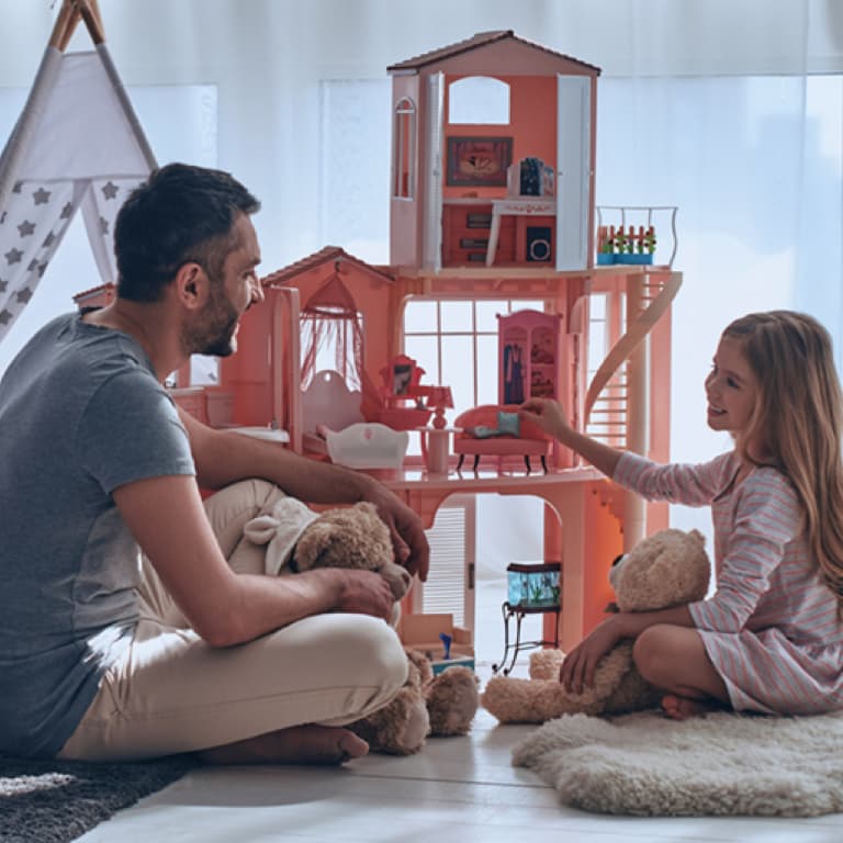 Father and daughter sitting on the floor with teddies and enjoying playtime next by the dollhouse.