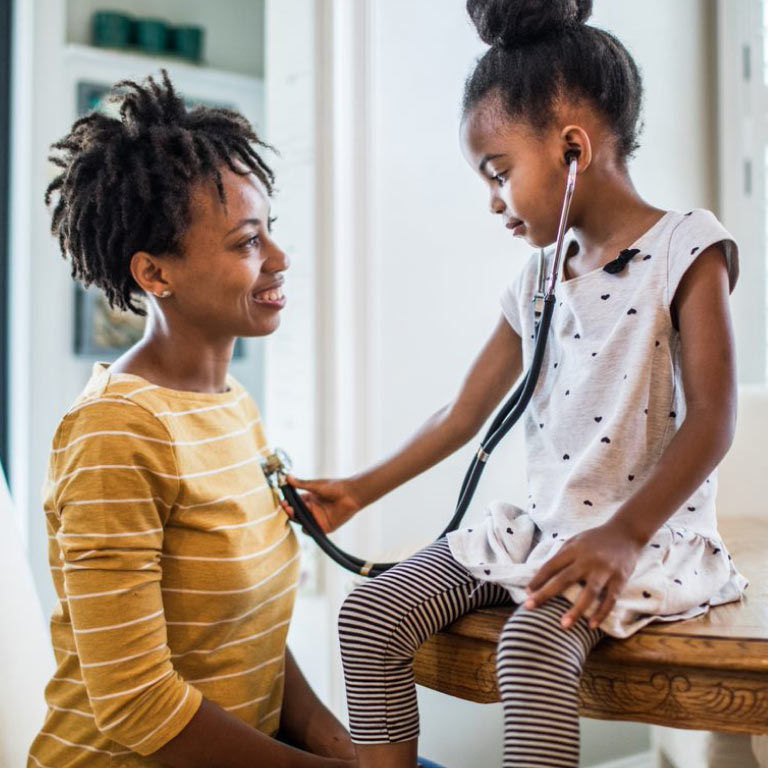 Young mother and daughter at home, with daughter using a stethoscope to listen to her mother’s heartbeat.