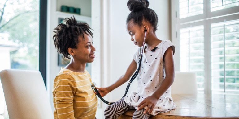 Young mother and daughter at home, with daughter using a stethoscope to listen to her mother’s heartbeat.