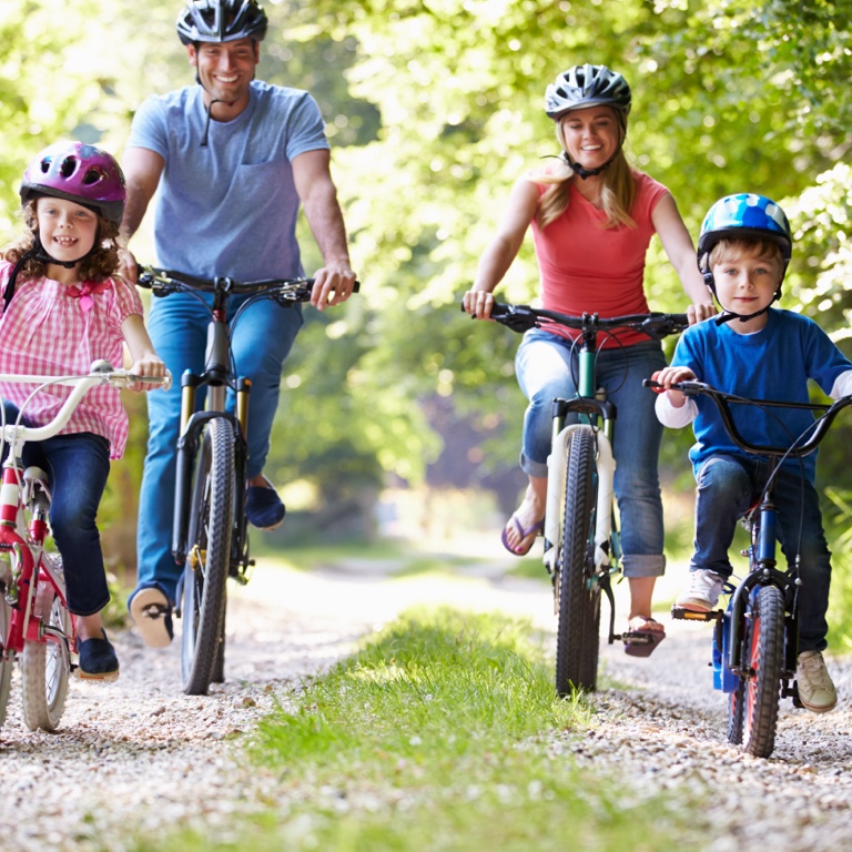 Happy mom and dad riding bicycles outdoors with their two children riding their bicycles ahead of their mother and father.