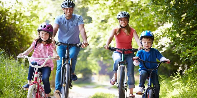 Happy mom and dad riding bicycles outdoors with their two children riding their bicycles ahead of their mother and father.