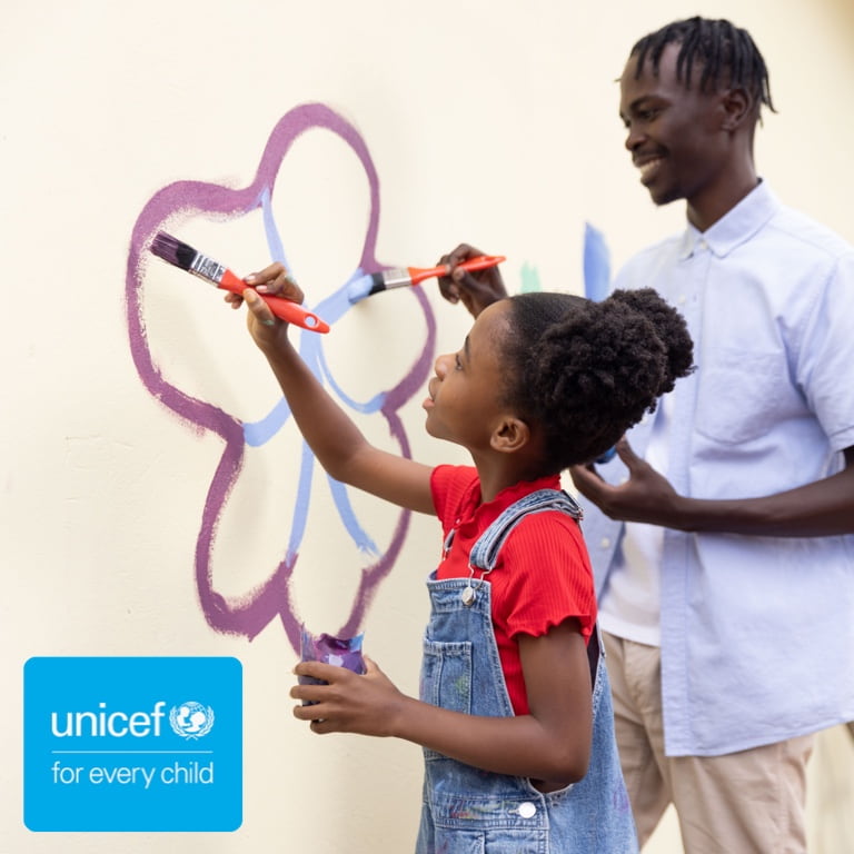 A UNICEF caregiver painting a flower with a young girl on a wall.