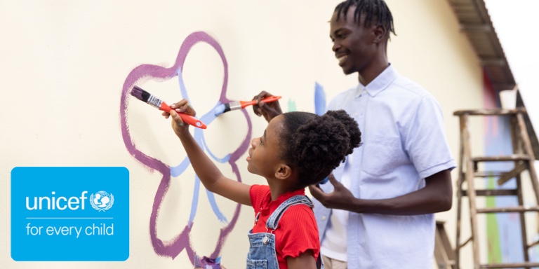A UNICEF caregiver painting a flower with a young girl on a wall.