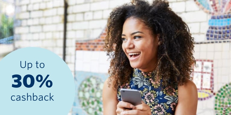 A curly-haired woman who has car and home insurance with Momentum Insure, holding her phone and excitedly reacting to the fact  that she gets rewarded up to 30% cashback for keeping safe through the Safety Returns rewards program. 