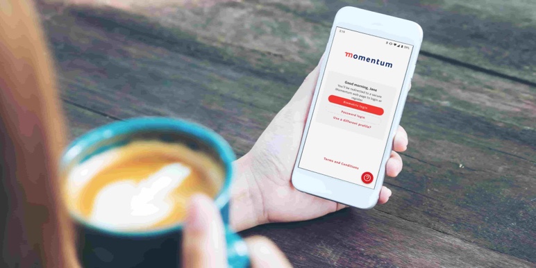 A lady with coffee in hand logging into the Momentum App to access her Traditional policy details.
