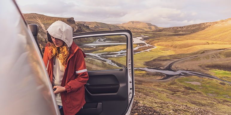 A Momentum Explorer benefit client outside her vehicle on a travel break, enjoying the adventure of a scenic landscape knowing she's covered by her car insurance to explore and travel.