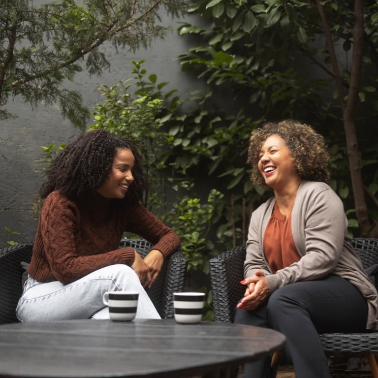 Two women enjoying a warm conversation over coffee in a garden setting, representing the approachable and personal support you can expect from a Momentum financial adviser.