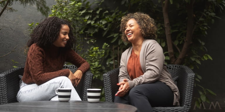 Two women enjoying a warm conversation over coffee in a garden setting, representing the approachable and personal support you can expect from a Momentum financial adviser.