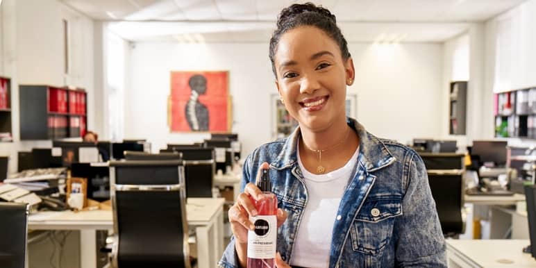  #MomentumFutures. A young, optimistic woman sitting on top of her office desk smiling ahead.