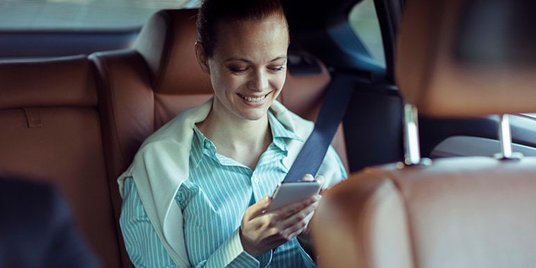 A young woman using the HomeDrive facility through Momentum Insure while sitting in the back seat of the car while the driver takes her safely home.