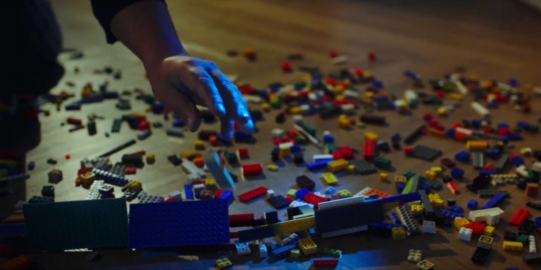 A man in pyjamas removing Lego blocks from under his feet.