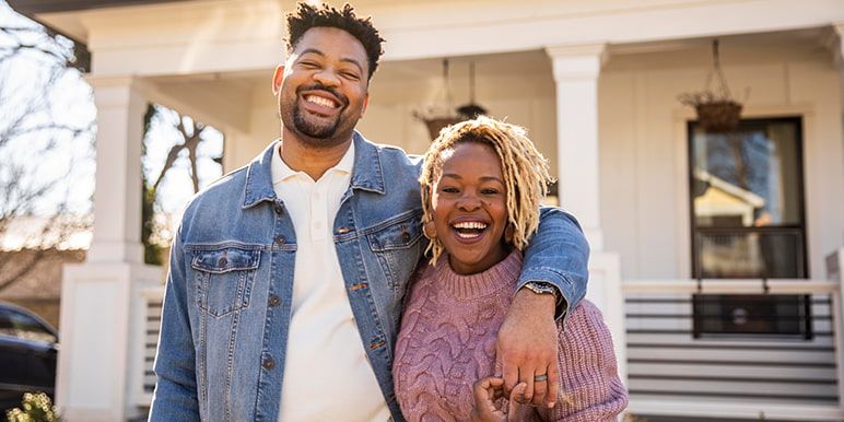 A couple standing in front of their home’s porch front excited about receiving 15% cashback on their paid premiums for remaining claim-free for 4 consecutive years with Momentum Insure's Momentum Rewarder.