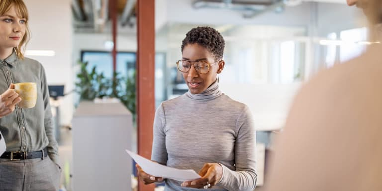 women standing in a modern open plan office having a discussion about a few documents.