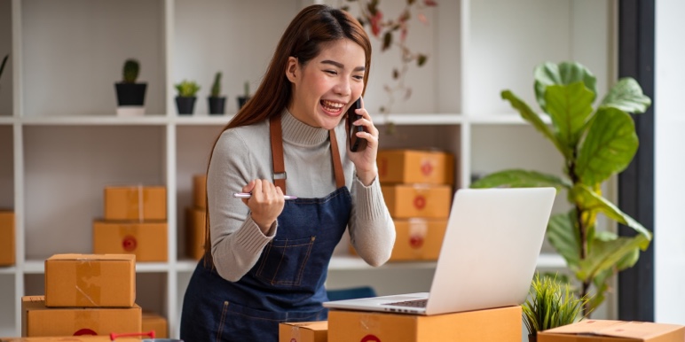 Small business owner standing excitedly in front of her laptop while on the phone.