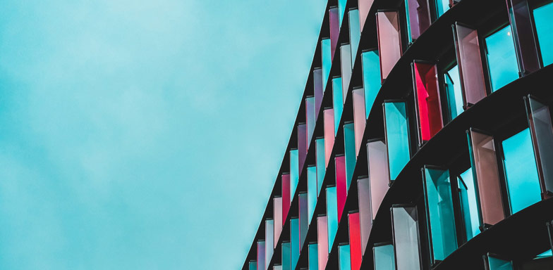 A modern multistory office building made with multi-colured glass in different shades of reds and blues, against a blue sky drop.