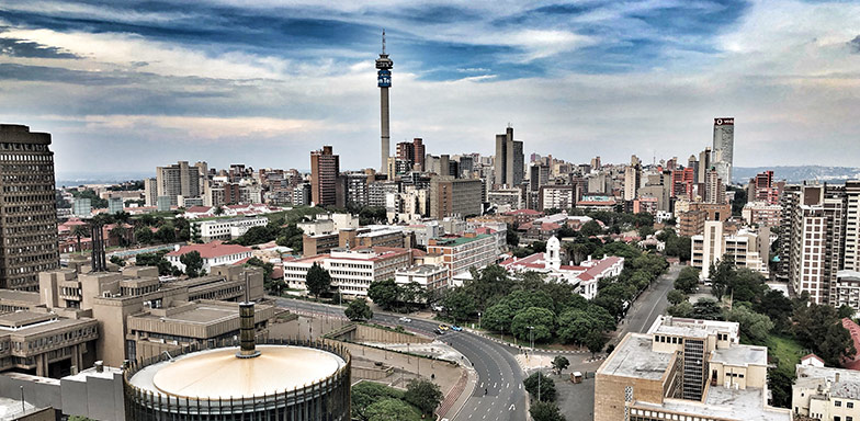 An aerial view of the Johannesburg city skyline against a cloudy deep blue sky.