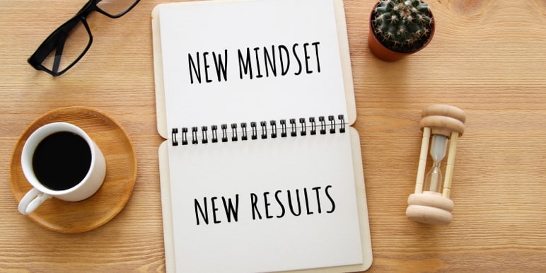 An open notepad placed on a work desk with the words “new mindset, new results” written on it.