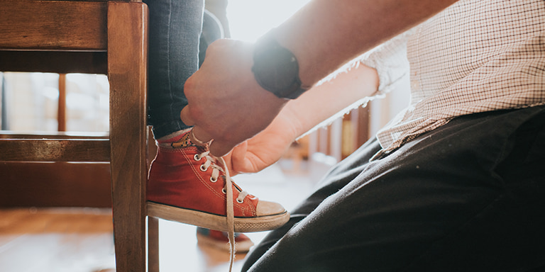 A father tying the red All-Stars of his little daughter while kneeling on the floor.