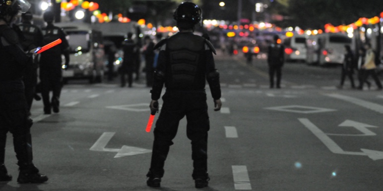 Police officers stand in the road to block off a mob of rioting people.
