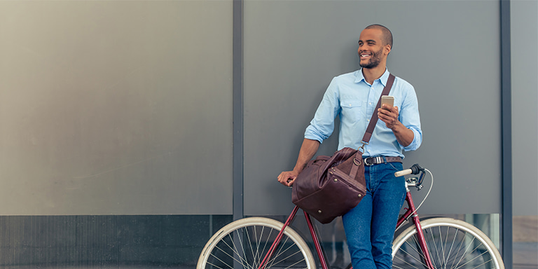 A man leaning on his bike against a grey wall as he gets a quote for Momentum Priceless car and home insurance on his phone.
