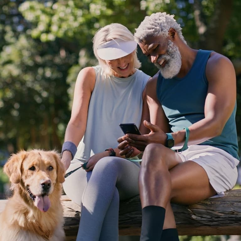 A fit retired couple in the outdoors enjoying a worry-free retirement. They’re confident in their healthcare planning while checking their retirement savings on a mobile phone.