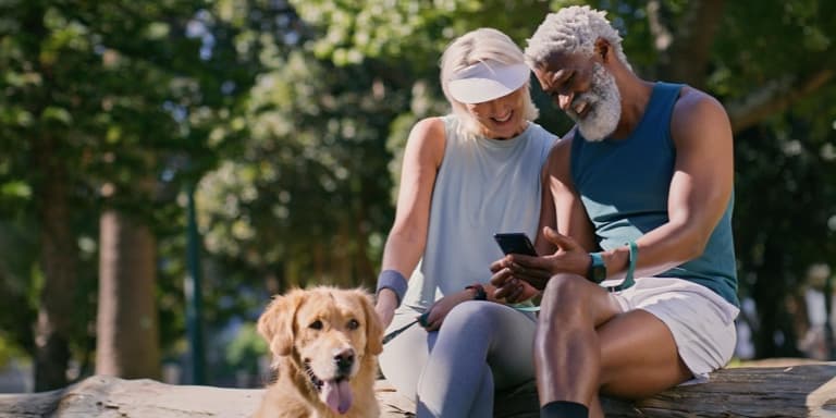 A fit retired couple in the outdoors with their dog sitting on a log after exercise, confident in their retirement savings and healthcare planning with an Investo Retirement Annuity.