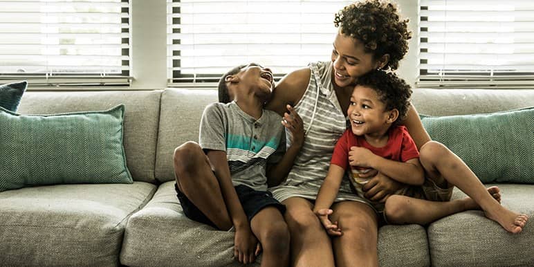 A mum and her 2 children sitting on the couch all embracing and keeping close to her.