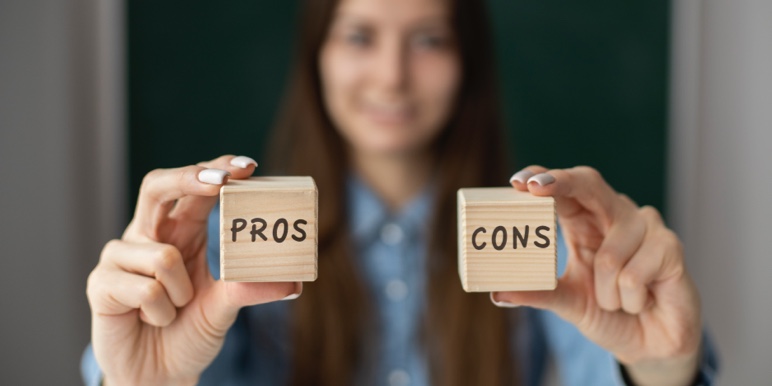 Woman standing with a small wooden block in each hand with one written “pros” and the other “cons”.