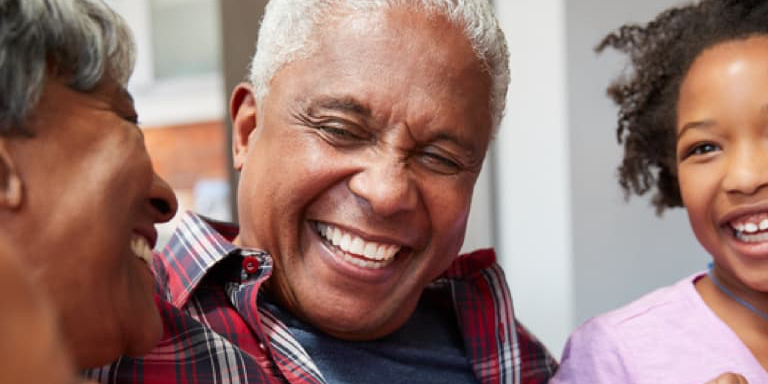 Grandparents sitting with their granddaughter on the grandfather's lap. They are all smiling.