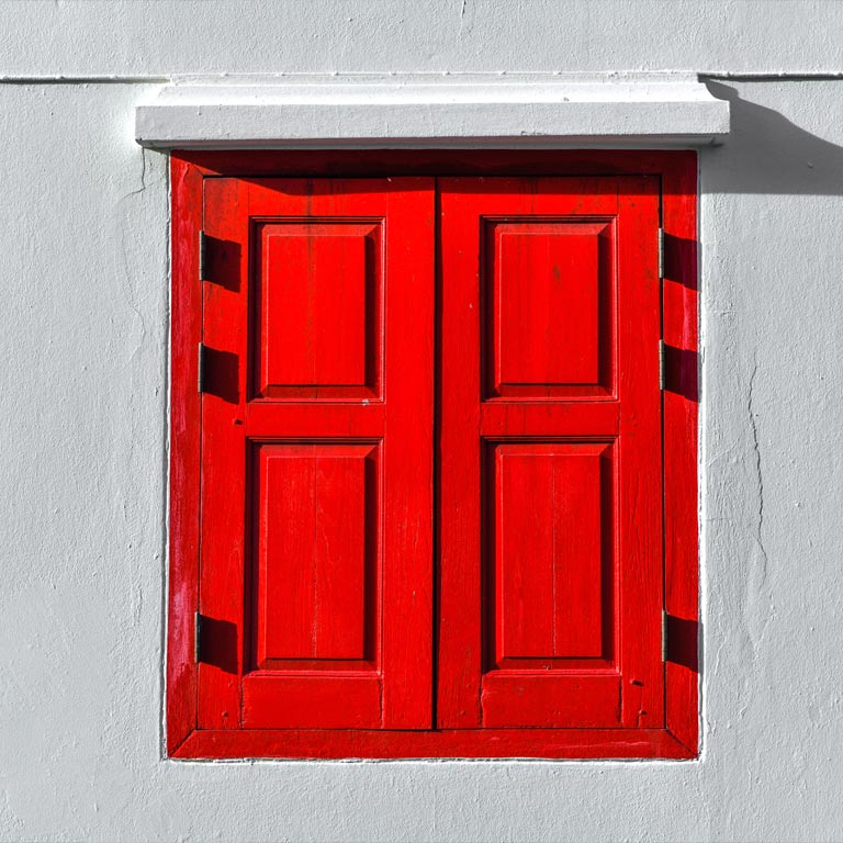 Wooden window shutters painted in red against a white wall.
