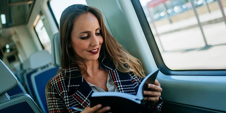 A woman sitting on a train heading safely to her destination while earning herself a safe day from Momentum Insure's Safe Dayz program, while reading her planner to prepare her for the rest of the day.