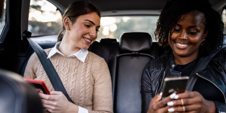 Two young females in a parked car looking at the passenger’s cell phone showing her completed Safety Score.