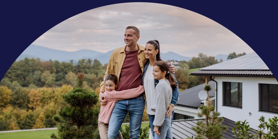 Mom and dad standing in front of their home with their two young daughters.