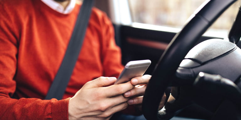 A man in the driver's seat in his car, accessing Momentum Insure's Safety Alert on his phone in a step-by-step video of how it works.