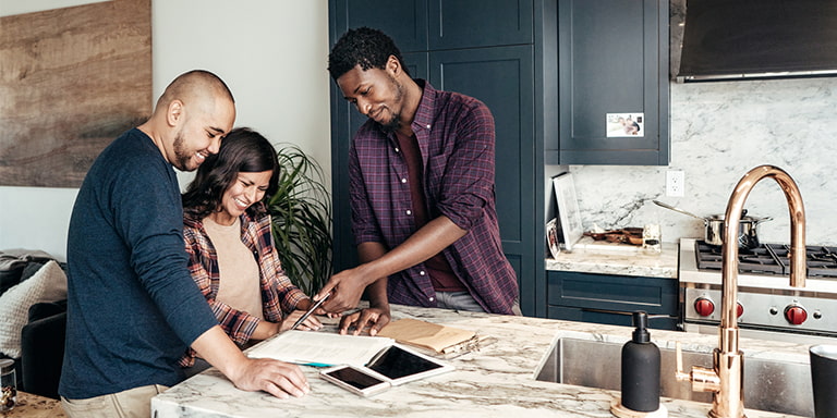 A couple in their house is reviewing their liability claim with their neighbour at a kitchen counter, feeling confident that they're legally and financially covered.