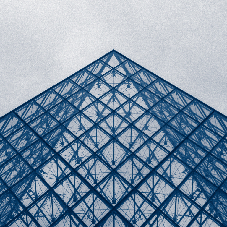 Top portion of a glass and steel pyramid structure - the design features a geometric grid of triangular glass panels framed by metal beams, creating a symmetrical pattern that converges to a point at the top.