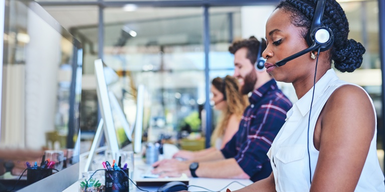 Call center staff, sitting at their work stations with their headphones on,  attending to client phone calls.
